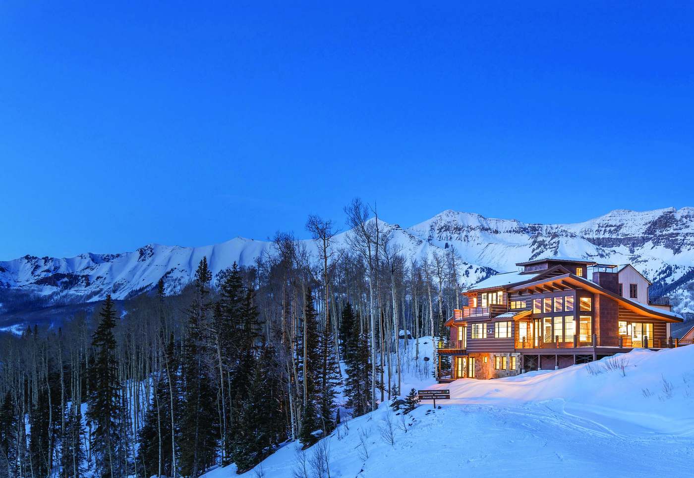 A custom residence at 240 Cortina Drive glowing at twilight, with the snow-covered San Juan Mountains behind it.